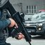 Imagem mostra um policial militar do BAEP (Batalhão de Ações Especiais de Polícia) da Polícia Militar do Estado de São Paulo (PMESP) com um fuzil e uma viatura ao fundo