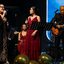 A imagem mostra músicos e cantoras se apresentando ao vivo no palco durante um evento musical