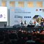 Pessoas sentadas enquanto assistem a apresentação de quatro pessoas em um palco