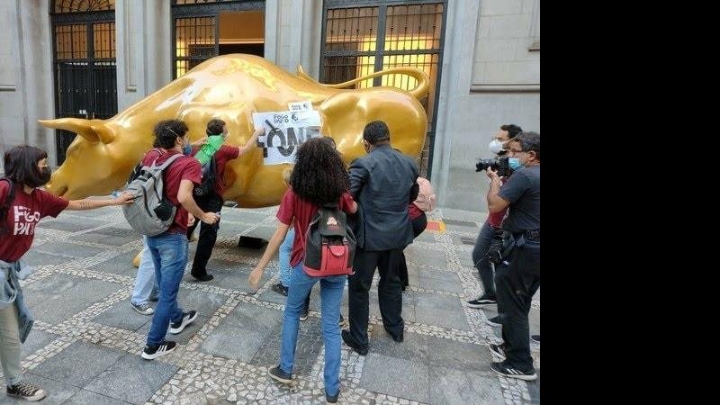 Ato foi registrado na manhã desta quarta-feira (17); seguranças tentaram impedir, mas não conseguiram de imediato Manifestantes colam cartazes em Touro de Ouro em São Paulo e fome é tema central Manifestantes colando cartazes em Touro de Ouro situado em Sã - Divulgação