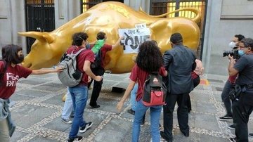 Ato foi registrado na manhã desta quarta-feira (17); seguranças tentaram impedir, mas não conseguiram de imediato Manifestantes colam cartazes em Touro de Ouro em São Paulo e fome é tema central Manifestantes colando cartazes em Touro de Ouro situado em Sã - Divulgação